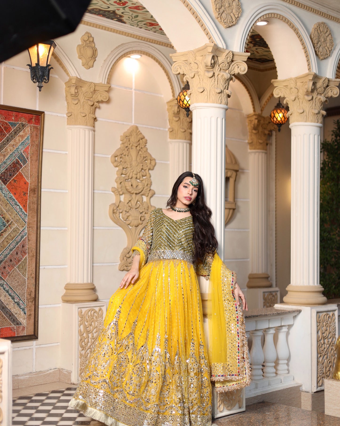 Woman in a traditional yellow and green outfit sitting in an ornate architectural setting.