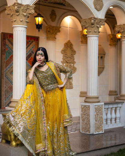 Woman in a yellow and gold traditional outfit standing in an ornate architectural setting.