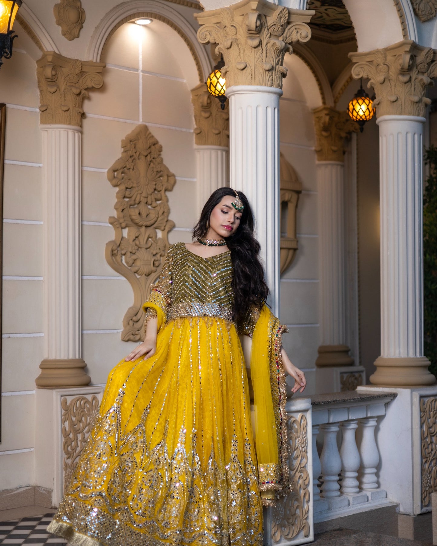 Woman in a yellow and gold traditional outfit standing in an ornate architectural setting.