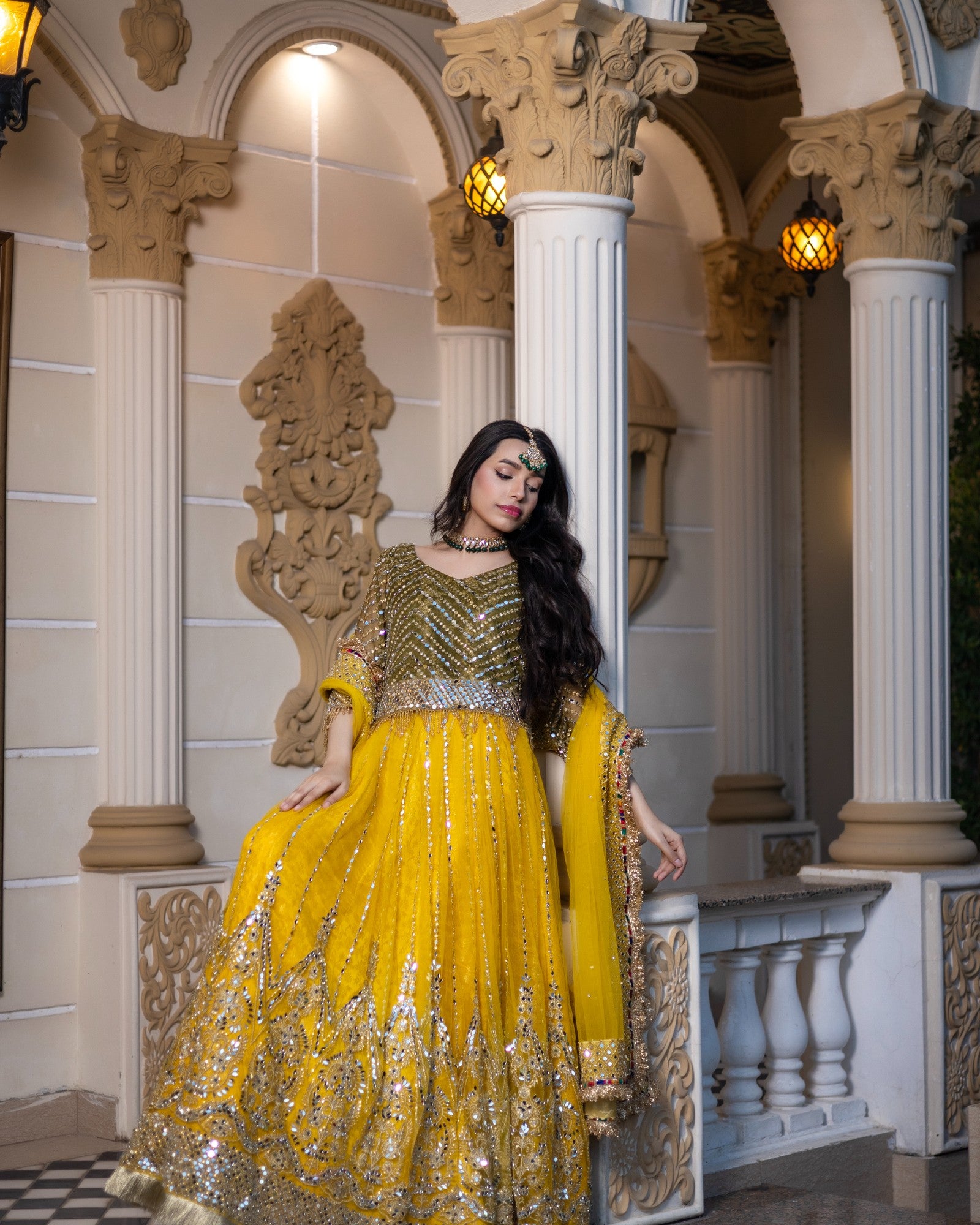 Woman in a yellow and gold traditional outfit standing in an ornate architectural setting.